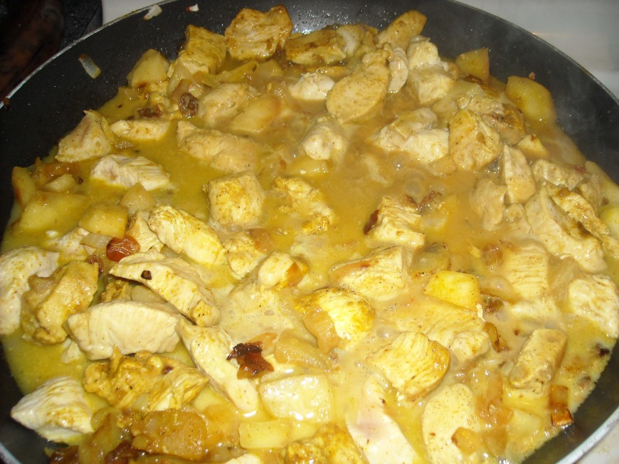 Curried chicken with  apples, raisins, onion, and spices simmering in coconut milk and chicken broth